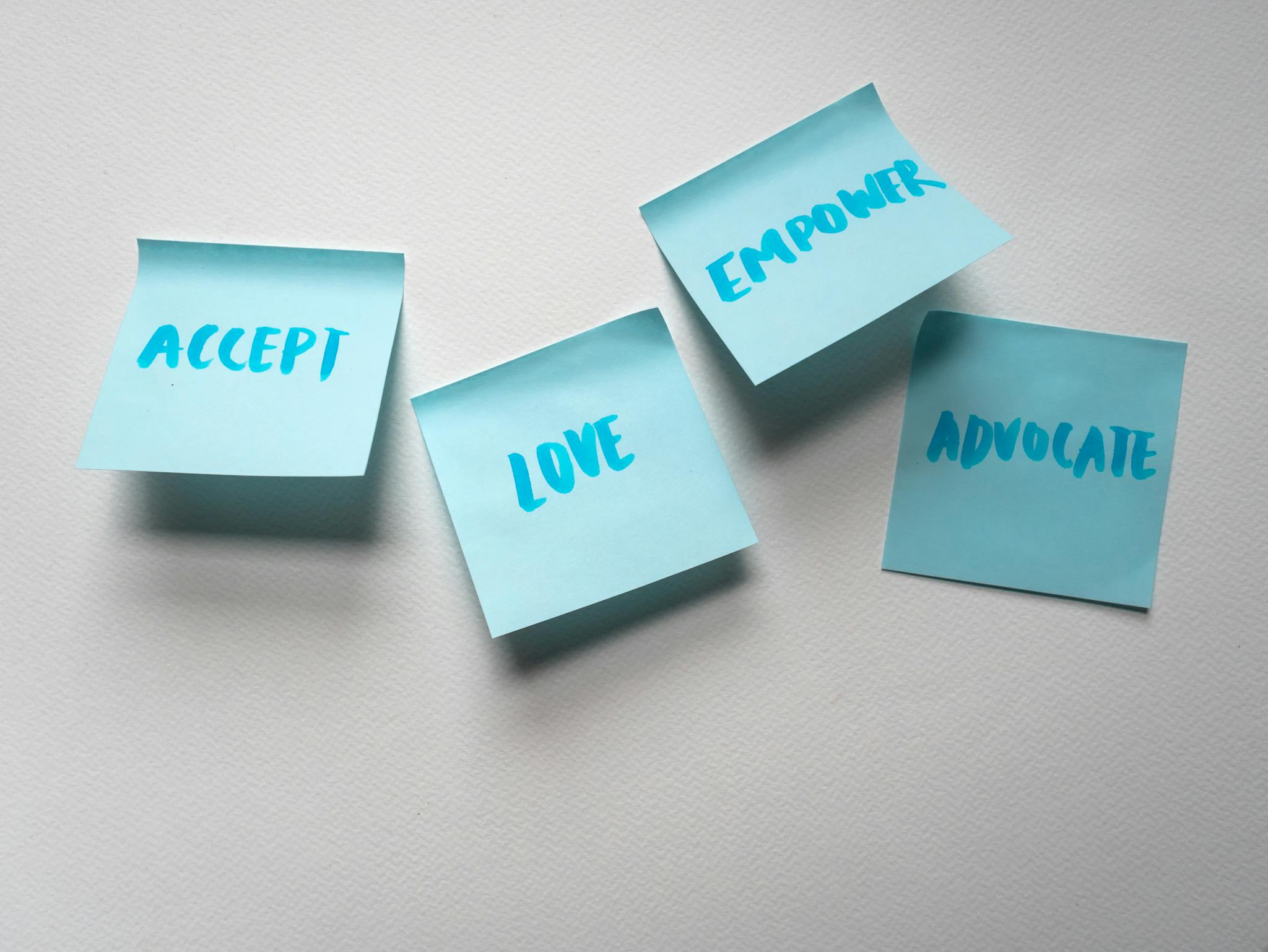 Four blue sticky notes with motivational words on a white surface.