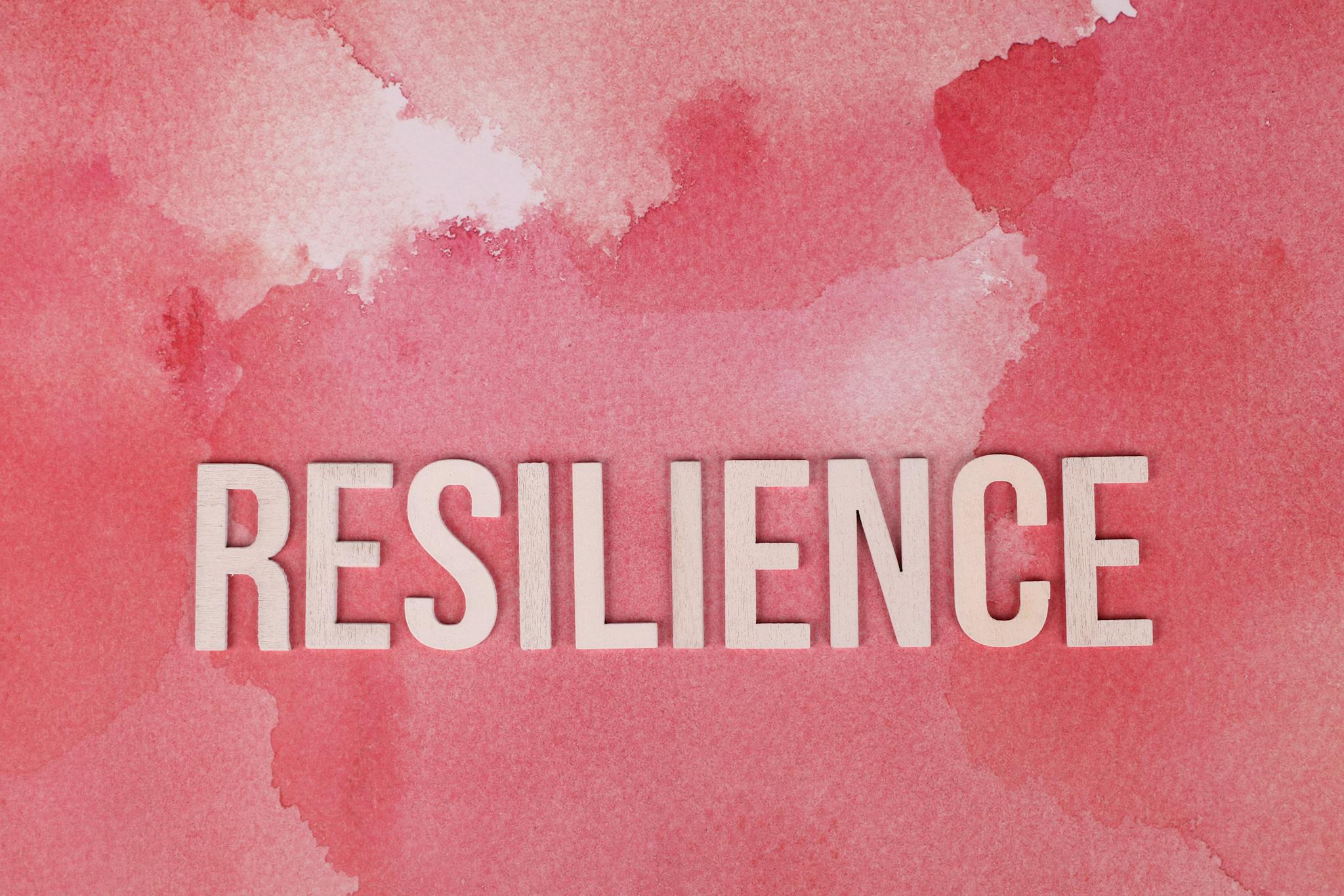 Word 'Resilience' on a pink watercolor background, symbolizing strength.
